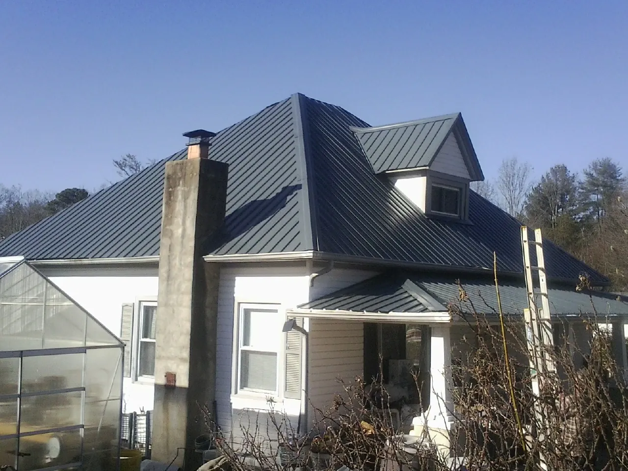 Dark blue standing seam metal roof on a white farmhouse with dormer — Slate & Tile Roof Repair by Roofing Brothers in Gaines