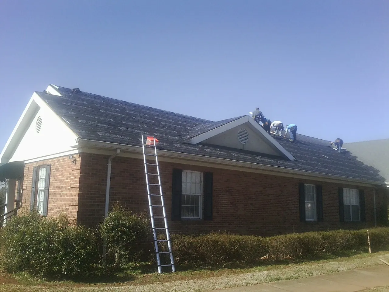 Crew tearing shingles off a brick ranch roof with a ladder set — Metal Roof Repair work by our crew in Gaines