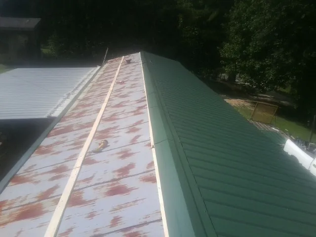 Old rusted panels beside newly installed green metal roofing — Wind Damage Roof Repair by Roofing Brothers in Gaines