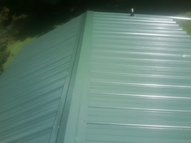 New green metal panels meeting at the ridge of a roof — Flat Roof Repair work by our crew in Gaines