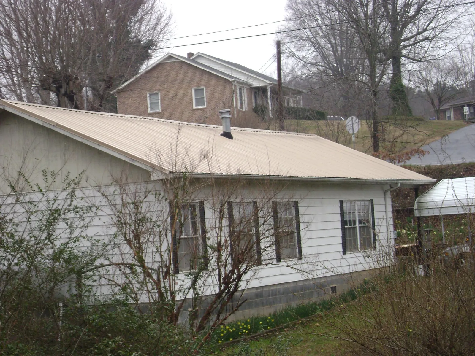 Tan metal roof on a white sided house set into a hillside — Commercial Roofing by Roofing Brothers in Gaines